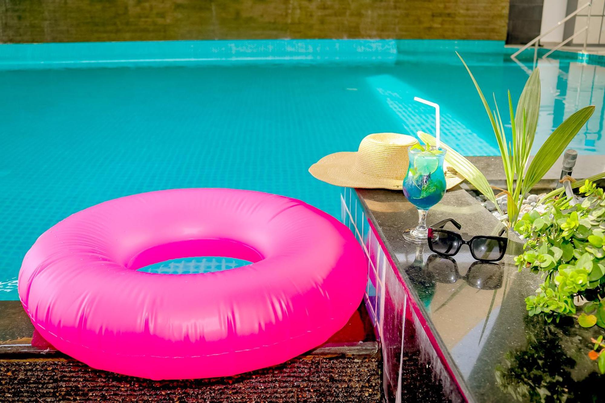 Lagoona Beach Luxury Resort And Spa Al Manamah Esterno foto The photo shows a vibrant and inviting scene by a swimming pool. In the foreground, there is a large pink inflatable float and a stylish straw hat. Next to the float, a refreshing cocktail in a glass is displayed, complete with a straw and garnishes.