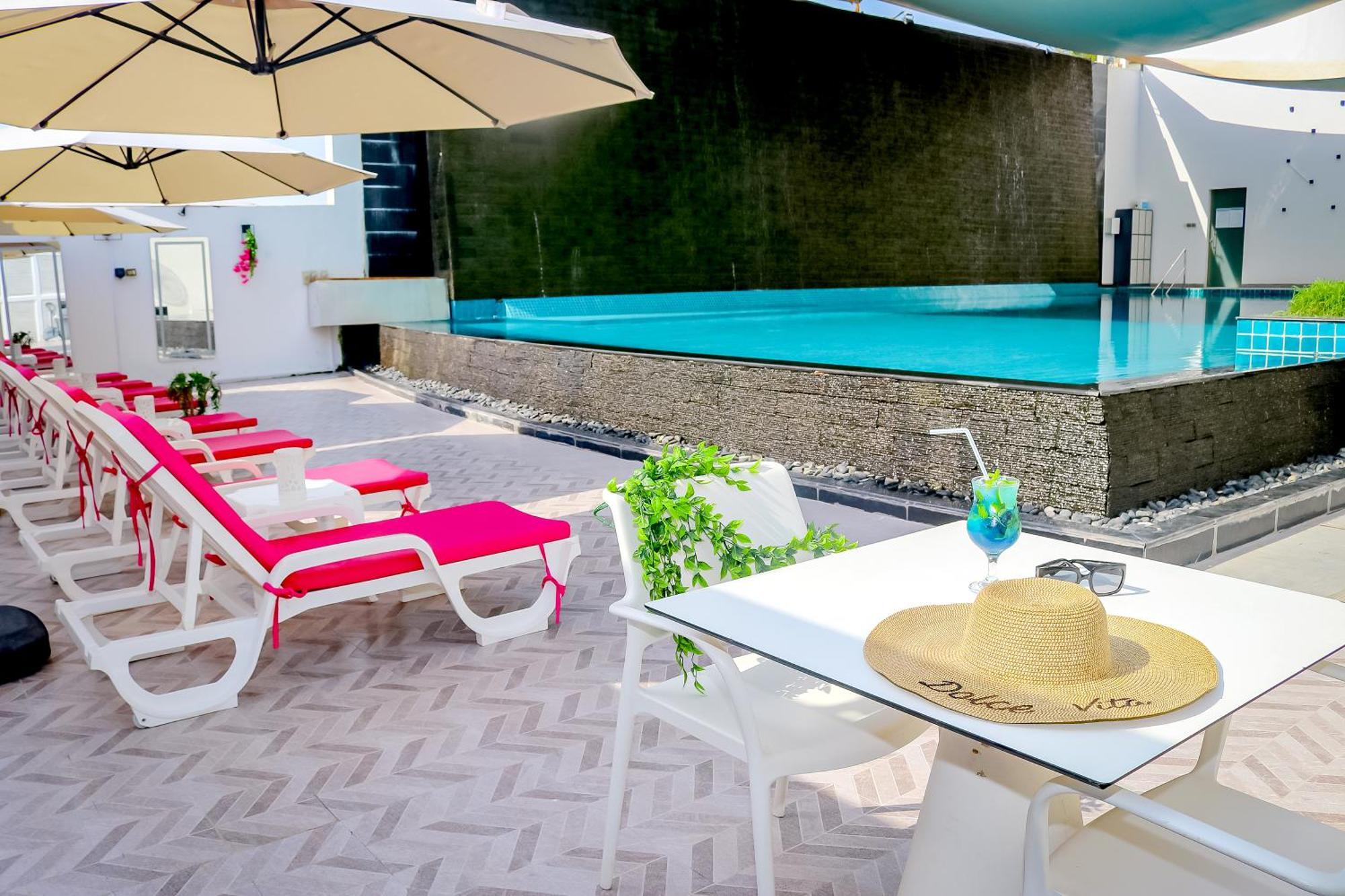 Lagoona Beach Luxury Resort And Spa Al Manamah Esterno foto The photo shows a sunny poolside area with bright red lounge chairs arranged neatly beside a swimming pool. There are large beige umbrellas providing shade. A small table is set up with a straw hat and a colorful drink, suggesting a relaxed, tropical