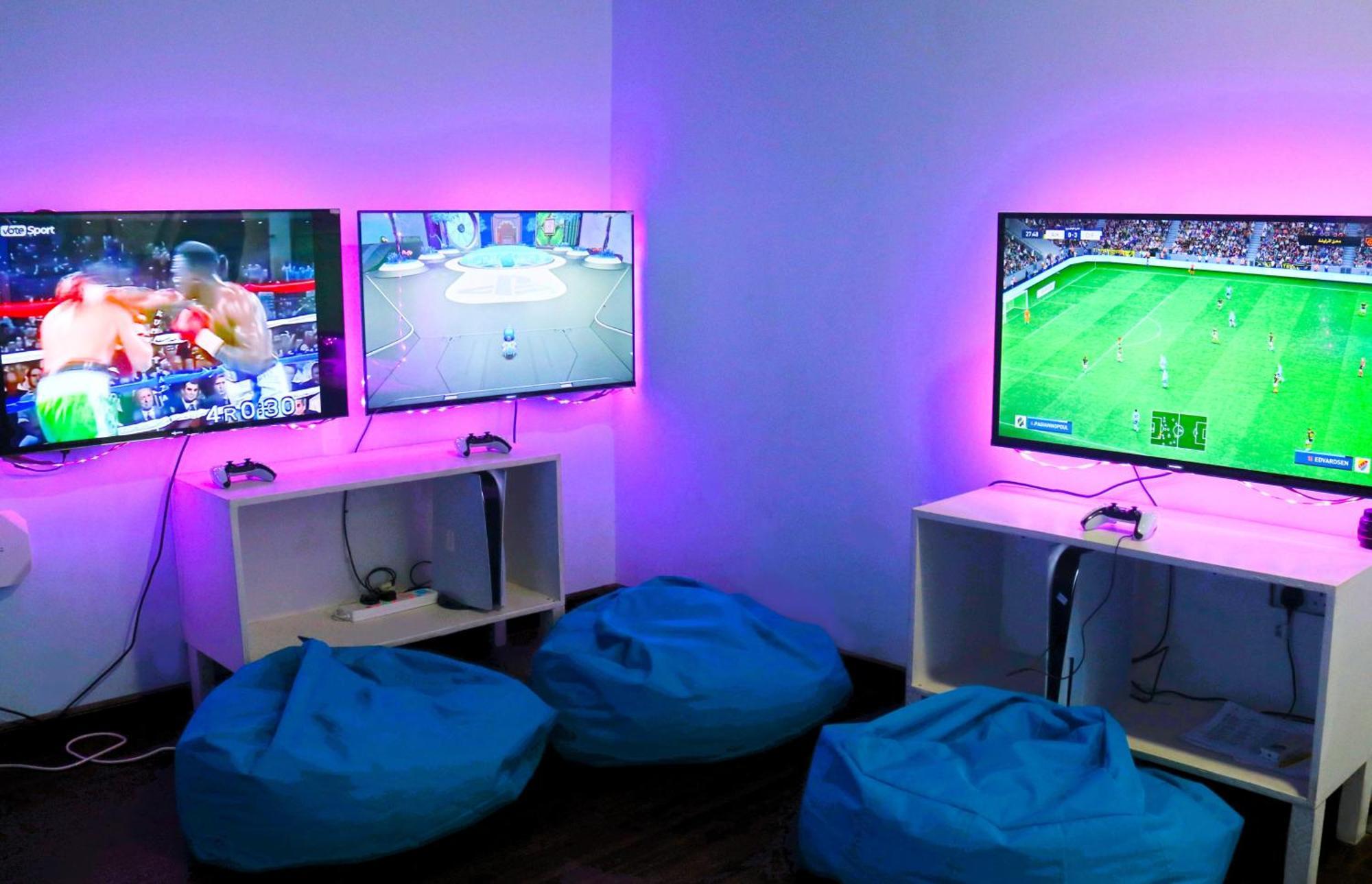 Lagoona Beach Luxury Resort And Spa Al Manamah Esterno foto The photo shows a gaming area featuring three televisions mounted on the wall, displaying different games. Two of the TVs are showing gaming scenes, with one depicting a boxing game and the other showing a vibrant game environment. The third TV displ
