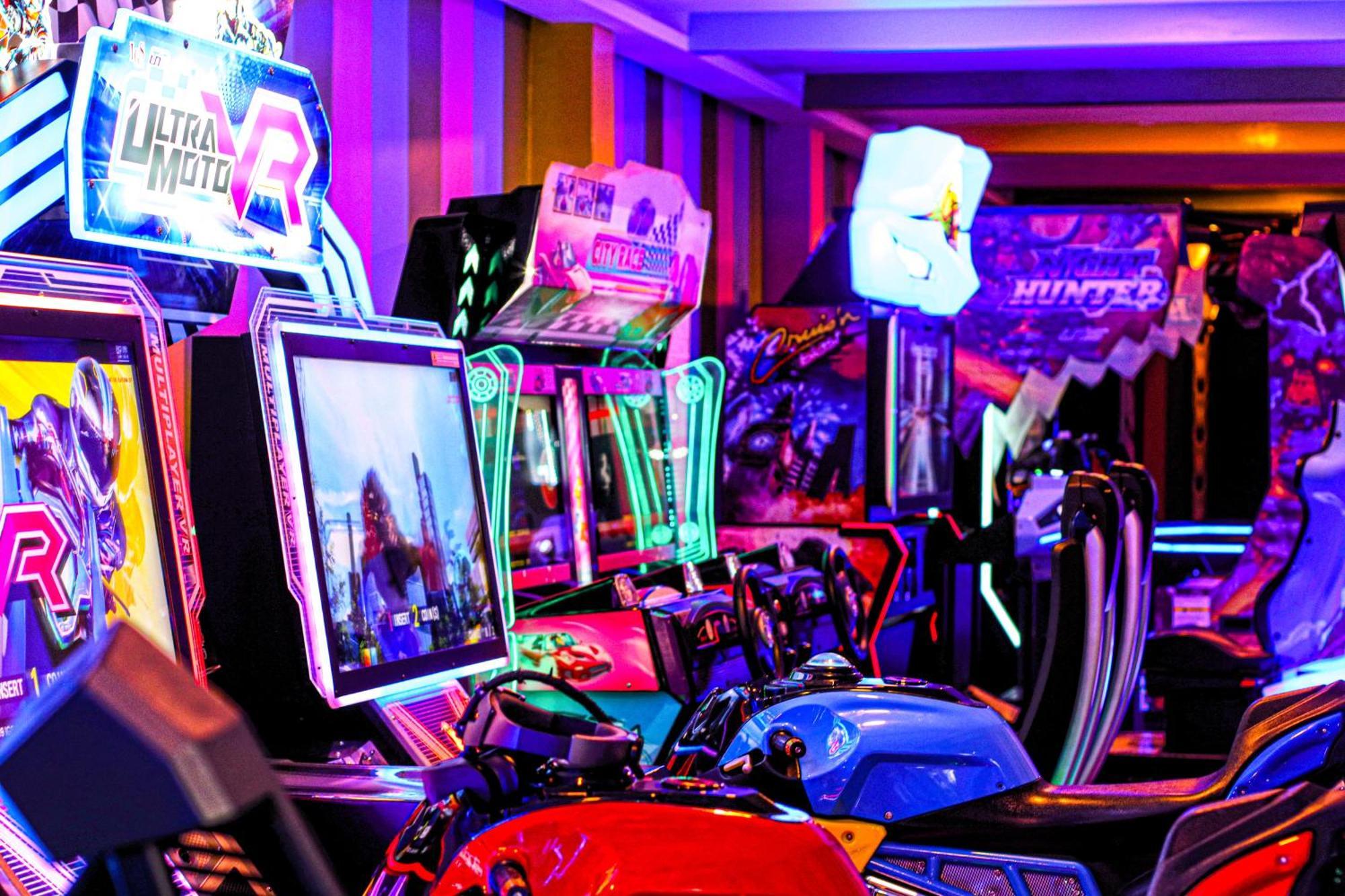 Lagoona Beach Luxury Resort And Spa Al Manamah Esterno foto The photo shows a vibrant arcade scene featuring various arcade gaming machines. The machines are lined up, showcasing colorful screens and bright, neon lights, creating an energetic atmosphere. Some machines appear to be racing games, as indicated b