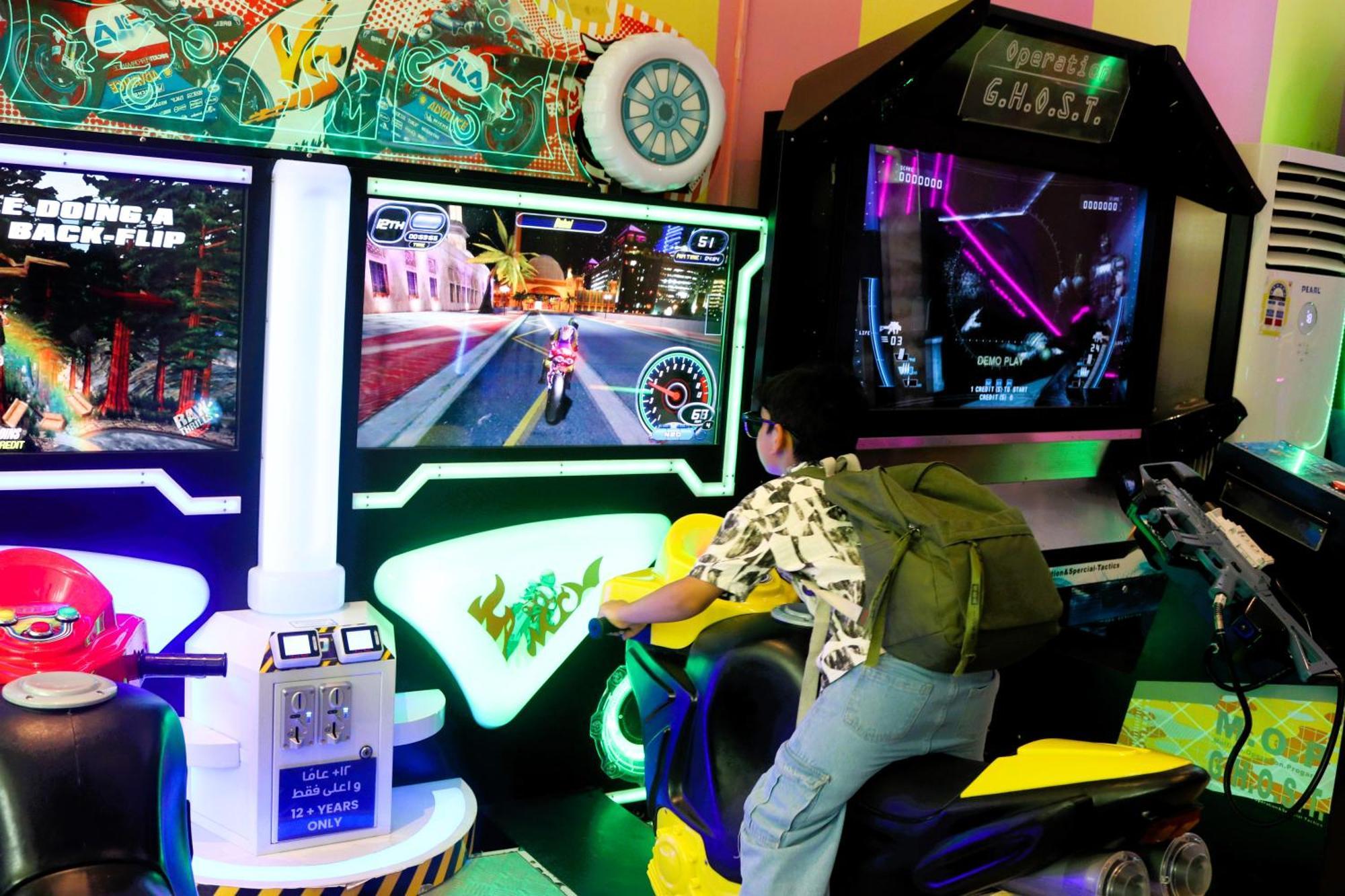 Lagoona Beach Luxury Resort And Spa Al Manamah Esterno foto The photo shows a person playing an arcade motorcycle racing game. They are seated on a motorcycle-shaped seat, actively engaging with the game displayed on the screen in front of them. The screen shows a vibrant racing scene with streets and colorfu