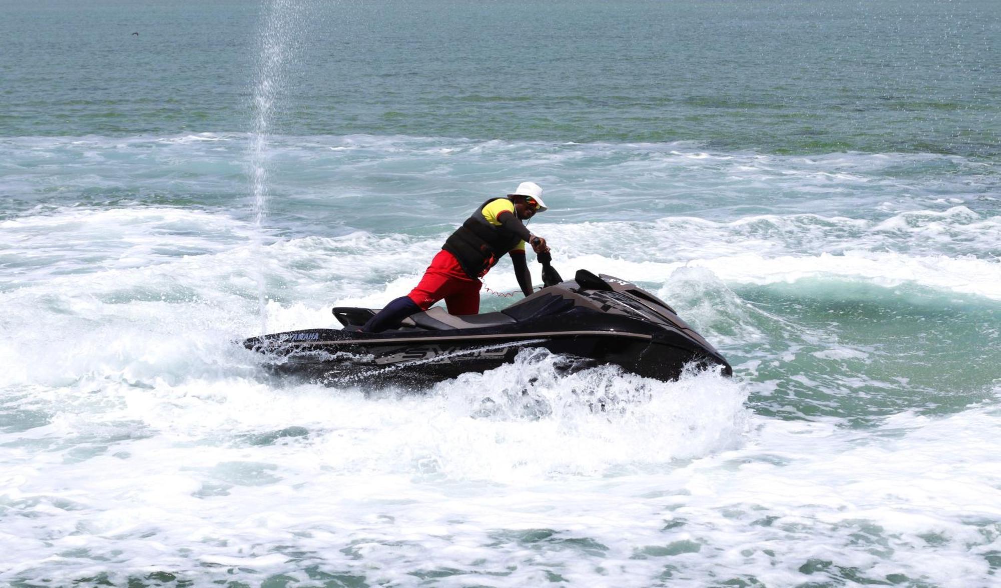 Lagoona Beach Luxury Resort And Spa Al Manamah Esterno foto The photo shows a person riding a jet ski on the water. The rider is positioned upright, leaning forward with one hand on the handlebars, while the jet ski creates splashes of white foam around it. The water appears choppy, likely due to the motion o