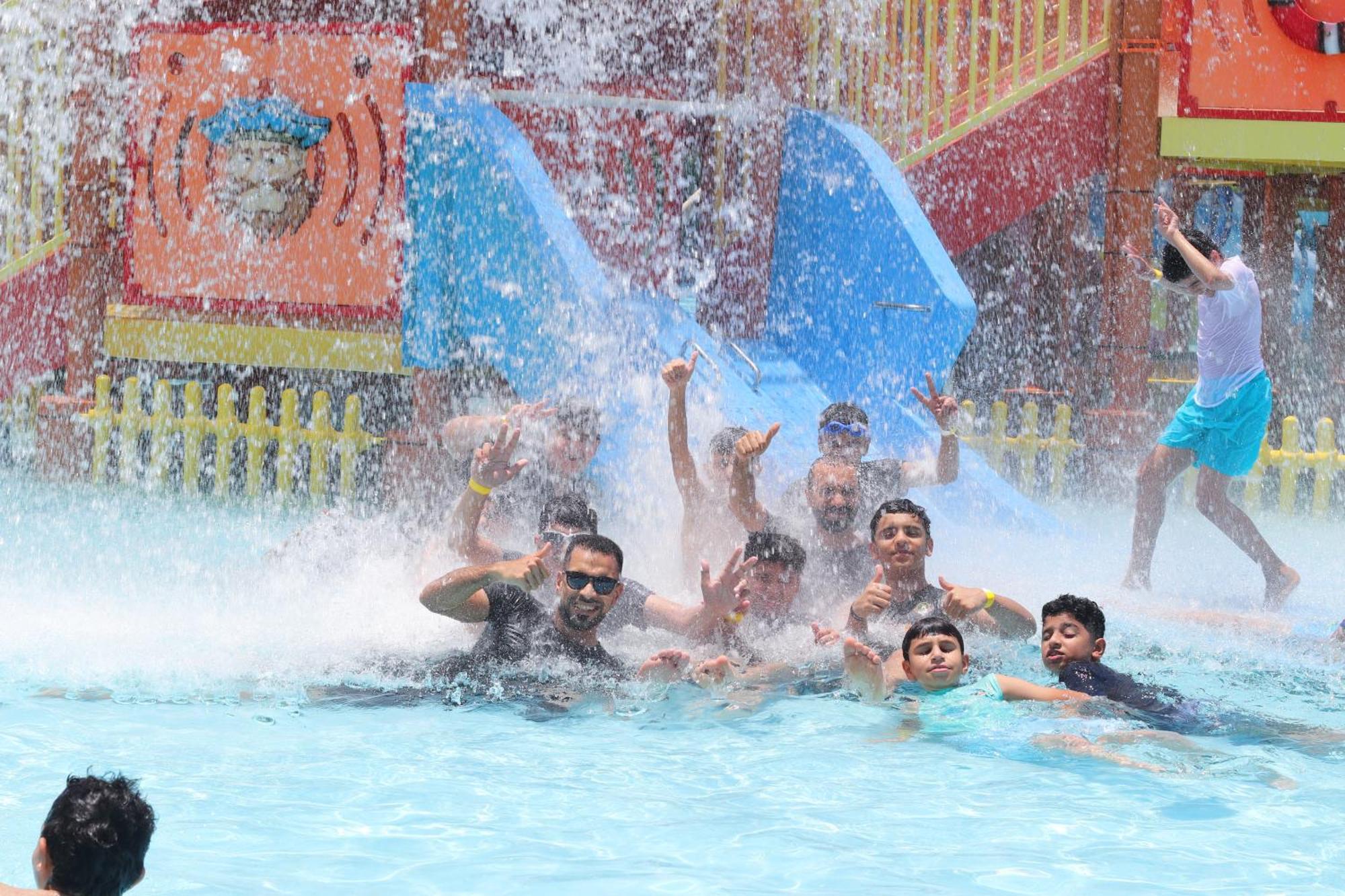 Lagoona Beach Luxury Resort And Spa Al Manamah Esterno foto The photo shows a lively scene at a water park or pool area. Several people, including adults and children, are enjoying themselves in the water, splashing and posing for the camera. Water is cascading down, creating a refreshing atmosphere. In the b