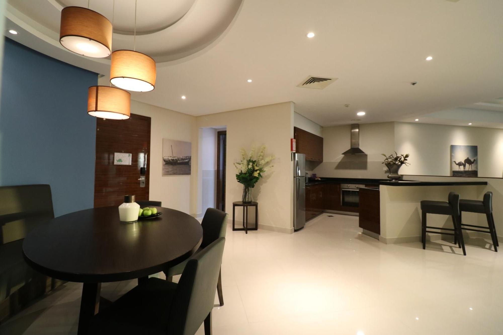 Lagoona Beach Luxury Resort And Spa Al Manamah Esterno foto The photo shows a modern, open-concept dining and kitchen area. On the left, there is a round dining table with black chairs, accompanied by a few decorative elements like a small vase and some fruit. The walls have a combination of light and dark to