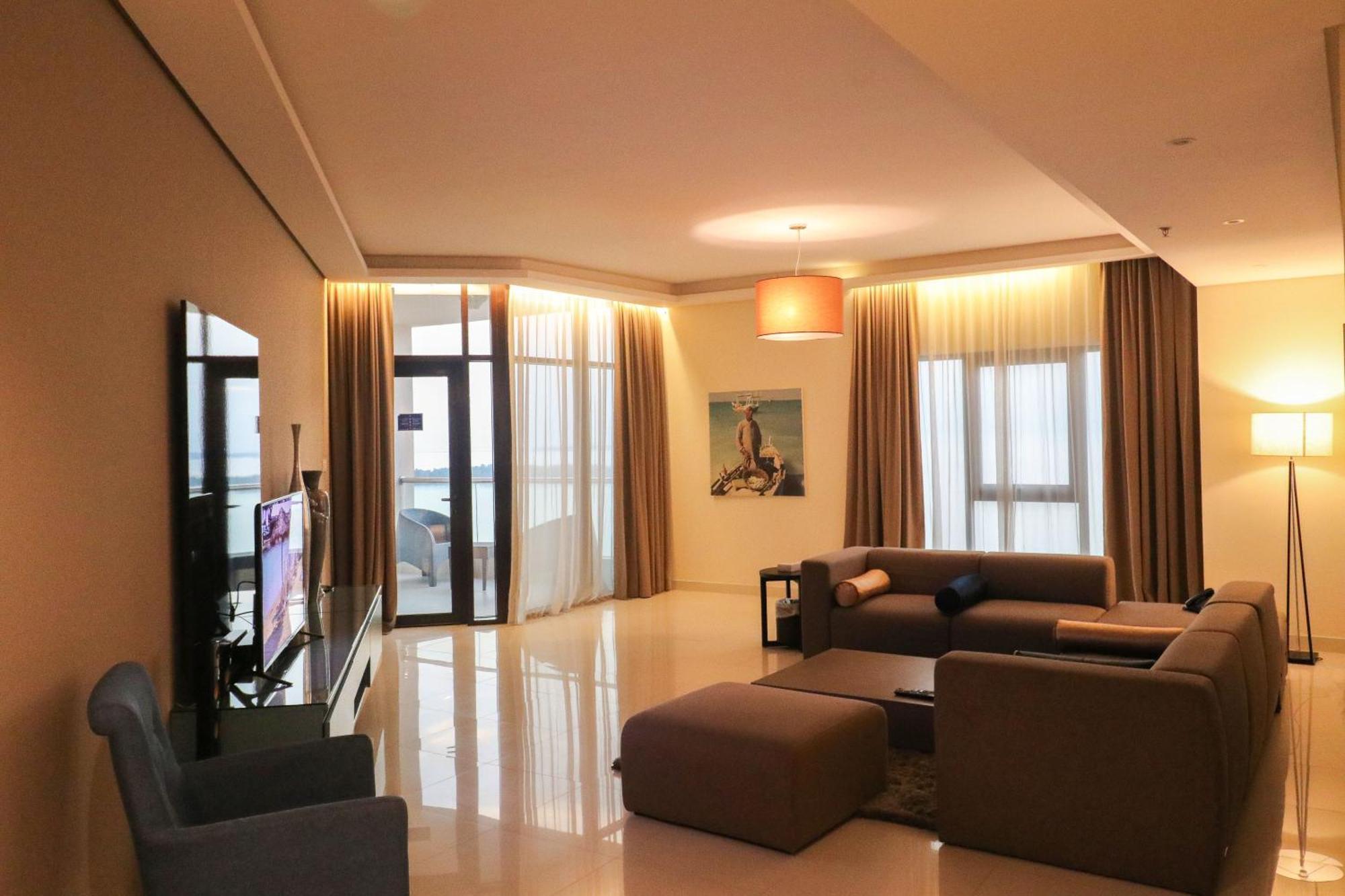 Lagoona Beach Luxury Resort And Spa Al Manamah Esterno foto The photo shows a modern living room with a spacious and elegant design. It features a large couch in neutral tones, a soft ottoman, and a stylish coffee table. The walls are painted in a light color, and there are large windows with sheer curtains a