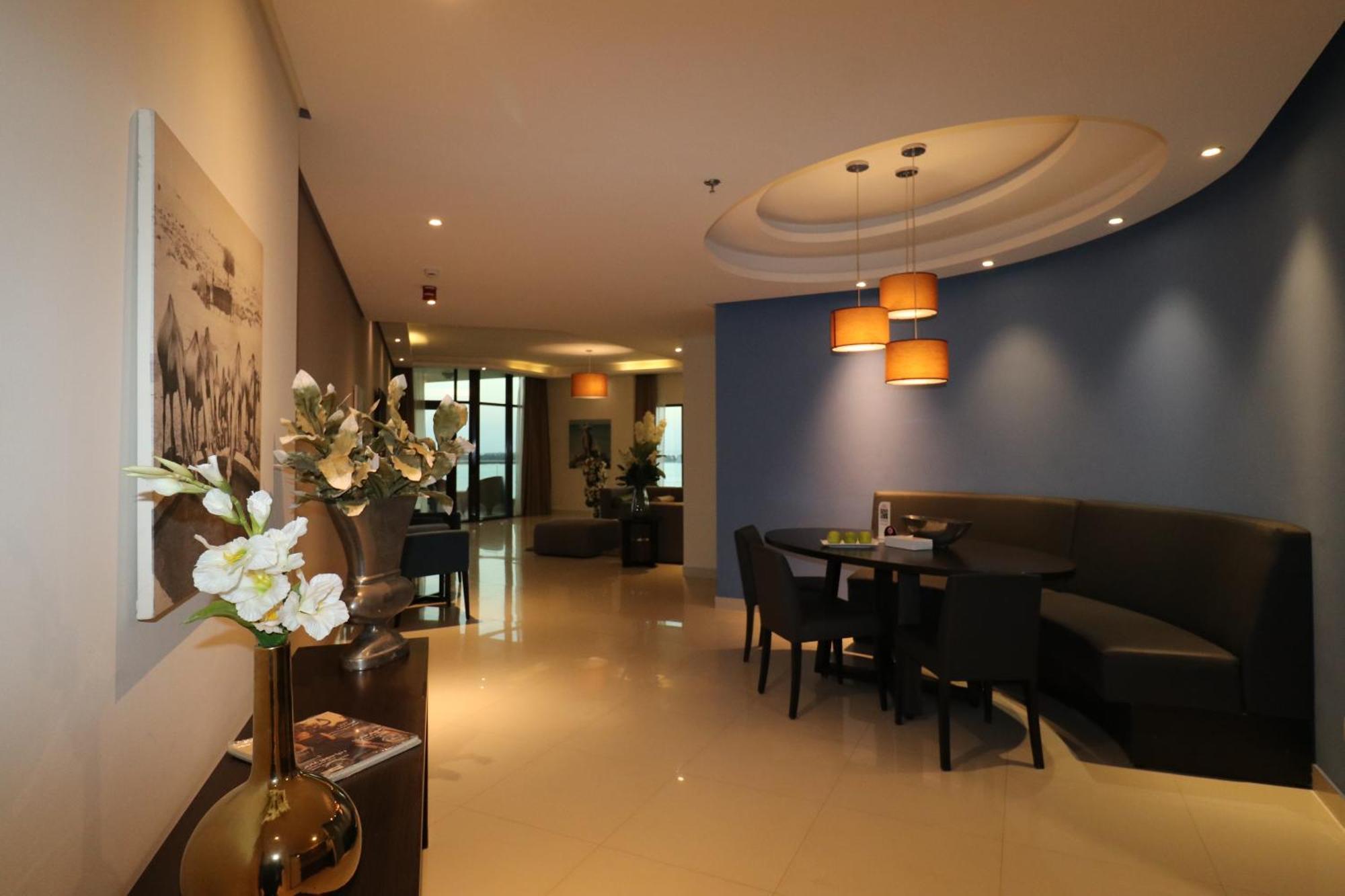 Lagoona Beach Luxury Resort And Spa Al Manamah Esterno foto The photo showcases an interior space, likely a modern lounge or reception area. It features a combination of soft lighting, neutral-colored walls, and decorative elements. There are elegant light fixtures hanging from the ceiling, and a curved blue 