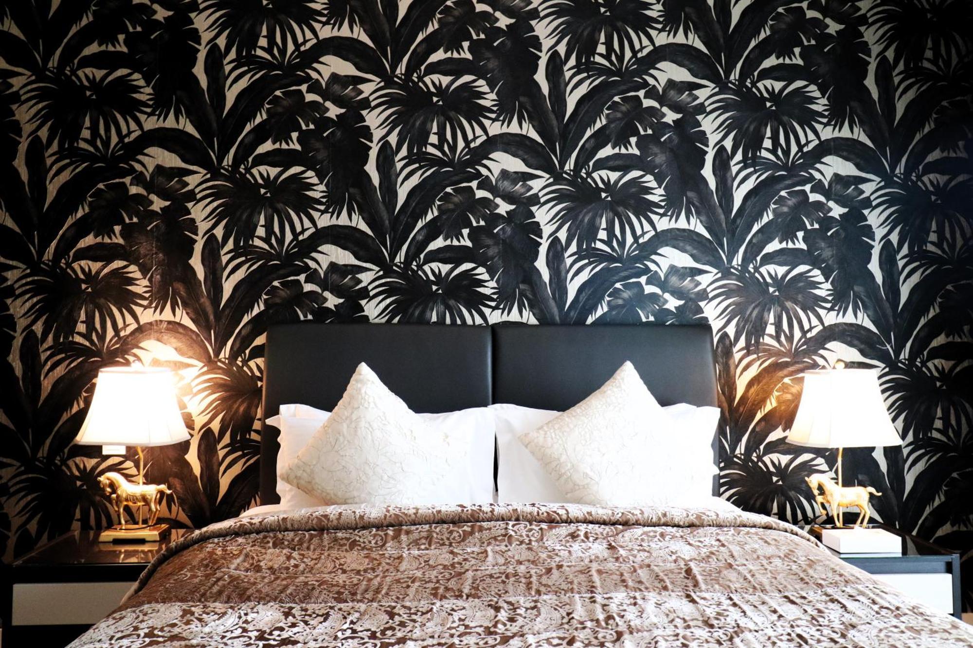 Lagoona Beach Luxury Resort And Spa Al Manamah Esterno foto The photo depicts a stylish bedroom featuring a distinctive wall covered in a black and white tropical foliage wallpaper. The bed has a modern black headboard and is adorned with white pillows, creating a clean and elegant look. A textured brown thro